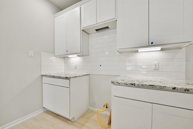 kitchen featuring white cabinets, backsplash, light hardwood / wood-style flooring, and light stone counters