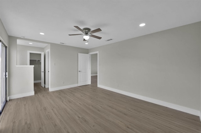 unfurnished bedroom featuring a closet, a walk in closet, ceiling fan, and light hardwood / wood-style flooring