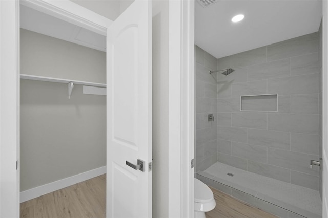 bathroom featuring tiled shower, hardwood / wood-style floors, and toilet