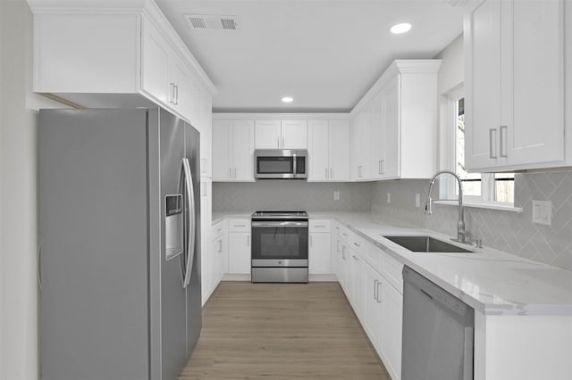 kitchen with backsplash, light stone counters, stainless steel appliances, sink, and white cabinets