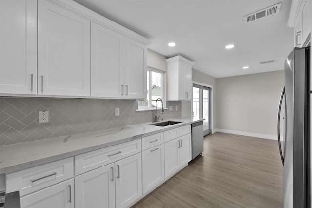 kitchen featuring appliances with stainless steel finishes, light stone counters, white cabinetry, and sink