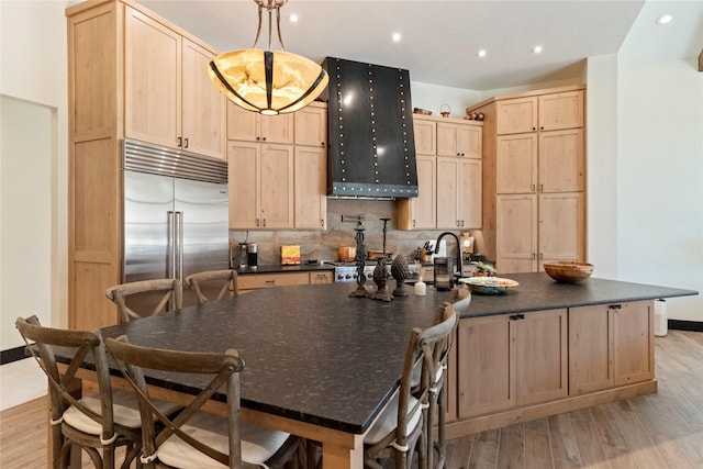 kitchen with built in refrigerator, light brown cabinets, hanging light fixtures, and light wood-type flooring