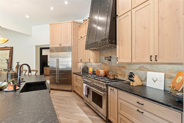 kitchen featuring high end appliances, sink, tasteful backsplash, custom range hood, and light wood-type flooring