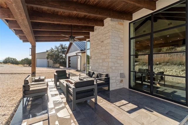 view of patio / terrace with a garage, ceiling fan, an outdoor structure, and an outdoor living space with a fire pit