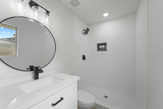 bathroom with a tile shower, vanity, and toilet