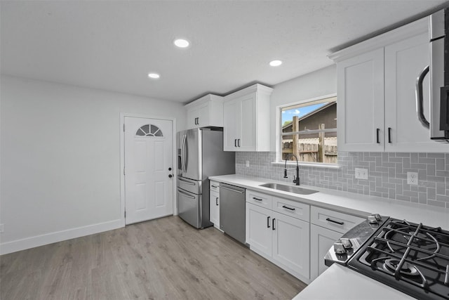 kitchen with sink, light hardwood / wood-style flooring, appliances with stainless steel finishes, tasteful backsplash, and white cabinetry