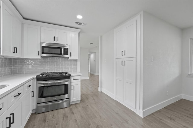 kitchen featuring white cabinets, light wood-type flooring, appliances with stainless steel finishes, and tasteful backsplash