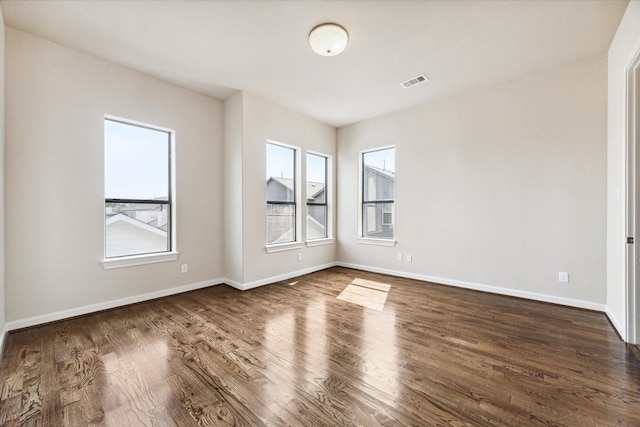 spare room featuring dark wood-style floors, visible vents, and baseboards