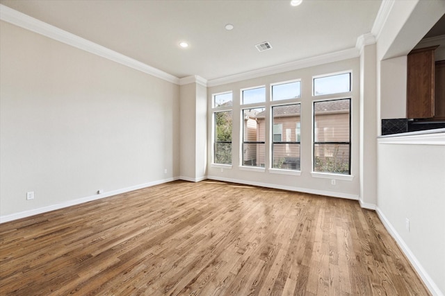 empty room featuring light wood-style floors, baseboards, visible vents, and ornamental molding