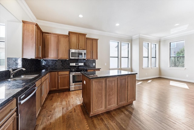 kitchen featuring tasteful backsplash, a kitchen island, ornamental molding, stainless steel appliances, and a sink