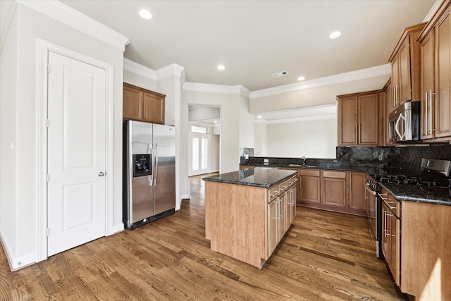 kitchen with sink, dark stone countertops, decorative backsplash, a kitchen island, and appliances with stainless steel finishes