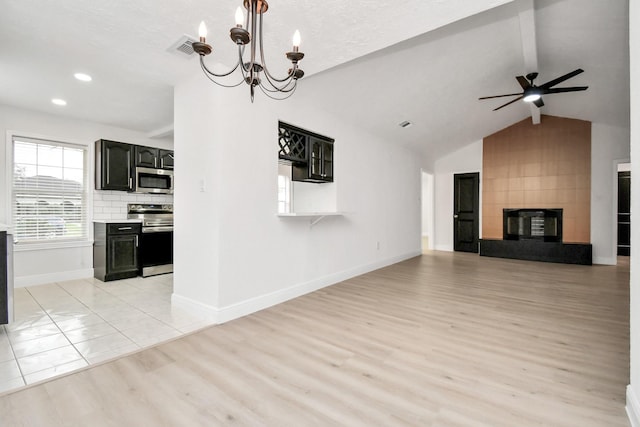 unfurnished living room with light wood-type flooring, ceiling fan with notable chandelier, vaulted ceiling, and a tiled fireplace