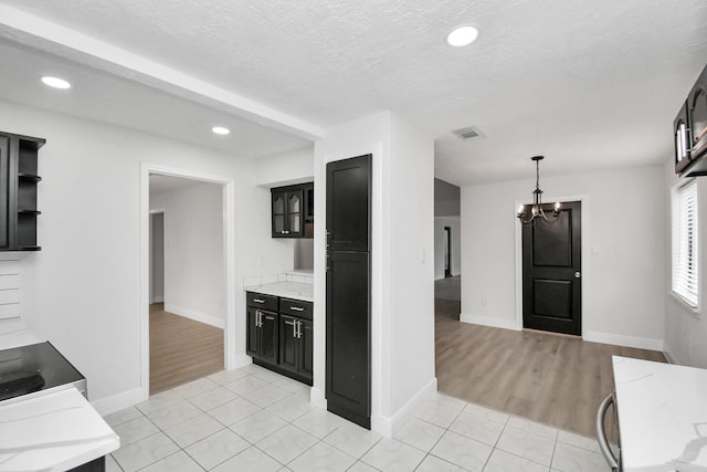 kitchen featuring a textured ceiling, decorative light fixtures, light tile patterned flooring, light stone counters, and a chandelier