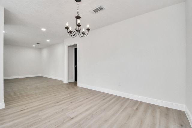 spare room featuring a chandelier and light hardwood / wood-style flooring