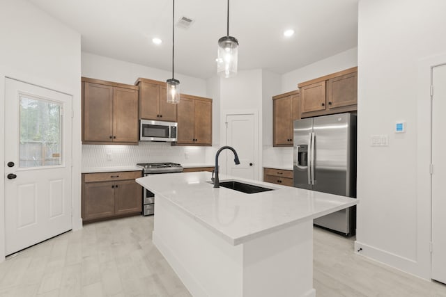 kitchen featuring sink, hanging light fixtures, tasteful backsplash, a center island with sink, and appliances with stainless steel finishes