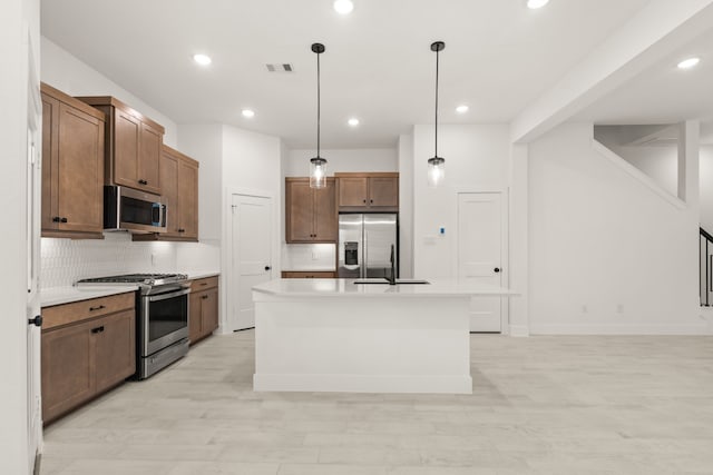 kitchen featuring sink, tasteful backsplash, decorative light fixtures, a kitchen island with sink, and appliances with stainless steel finishes