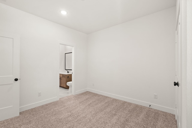 unfurnished bedroom featuring sink, light carpet, and ensuite bath