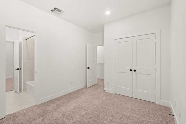 unfurnished bedroom featuring ensuite bath, light carpet, and a closet