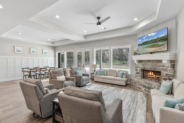 living room with ceiling fan, a raised ceiling, a fireplace, and light hardwood / wood-style flooring