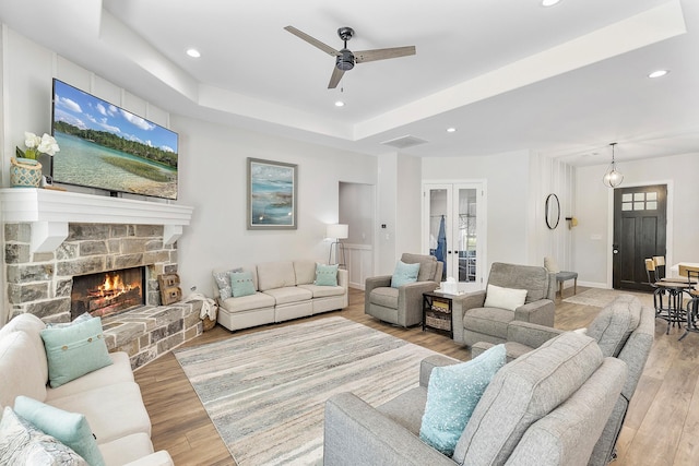 living room with a fireplace, light hardwood / wood-style flooring, a raised ceiling, and ceiling fan