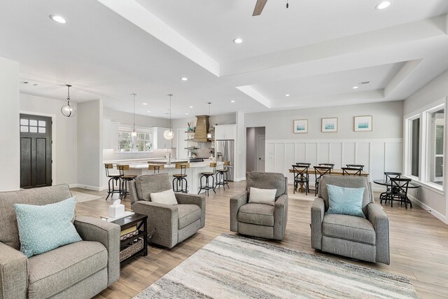 living room with ceiling fan, a raised ceiling, and light wood-type flooring