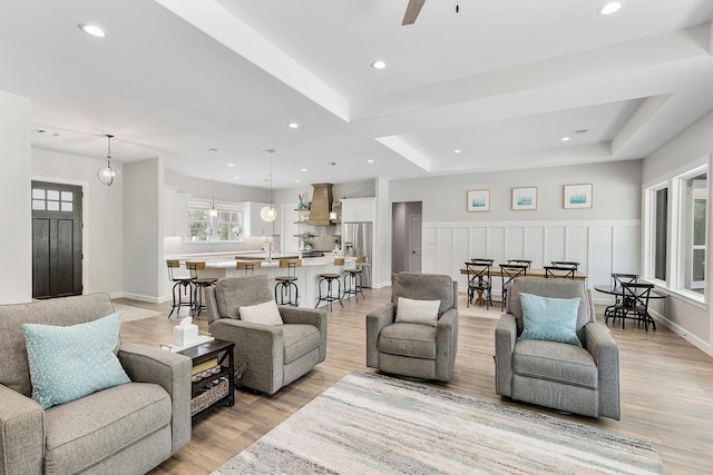 living room with a tray ceiling, ceiling fan, and light wood-type flooring