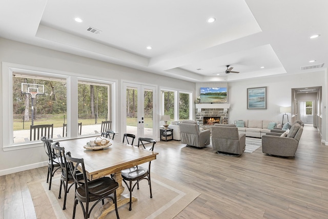 dining space featuring ceiling fan, light hardwood / wood-style floors, a fireplace, and a tray ceiling