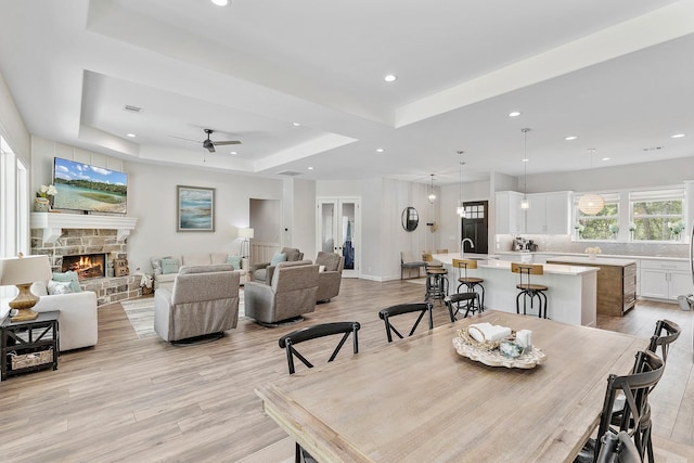 dining room with a fireplace, sink, ceiling fan, light hardwood / wood-style floors, and a raised ceiling