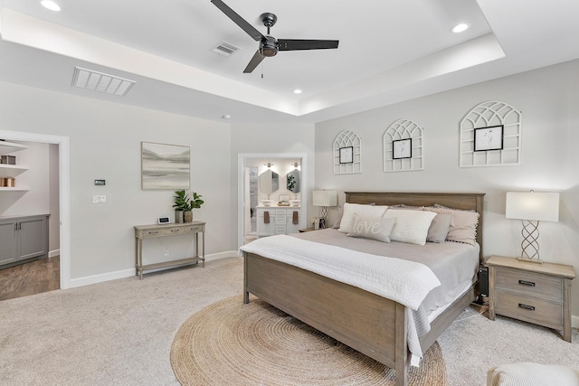 bedroom featuring ceiling fan, a raised ceiling, light colored carpet, and ensuite bath