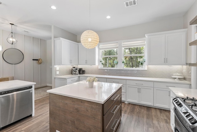 kitchen with white cabinetry, hanging light fixtures, appliances with stainless steel finishes, a kitchen island, and hardwood / wood-style flooring