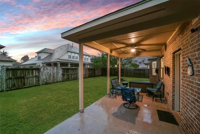 patio terrace at dusk featuring ceiling fan and a yard