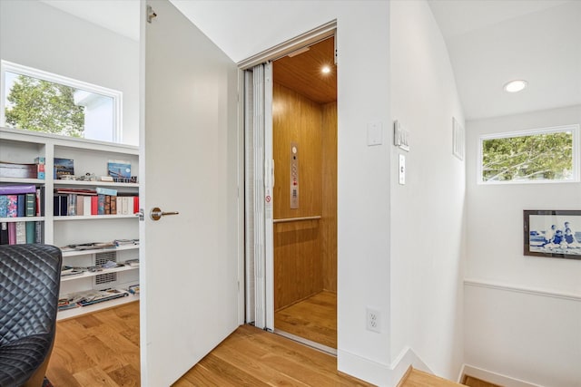 corridor with light hardwood / wood-style floors and lofted ceiling