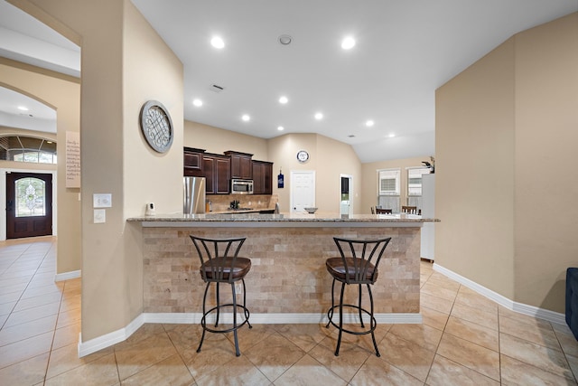 kitchen with a kitchen breakfast bar, kitchen peninsula, appliances with stainless steel finishes, light stone counters, and dark brown cabinetry