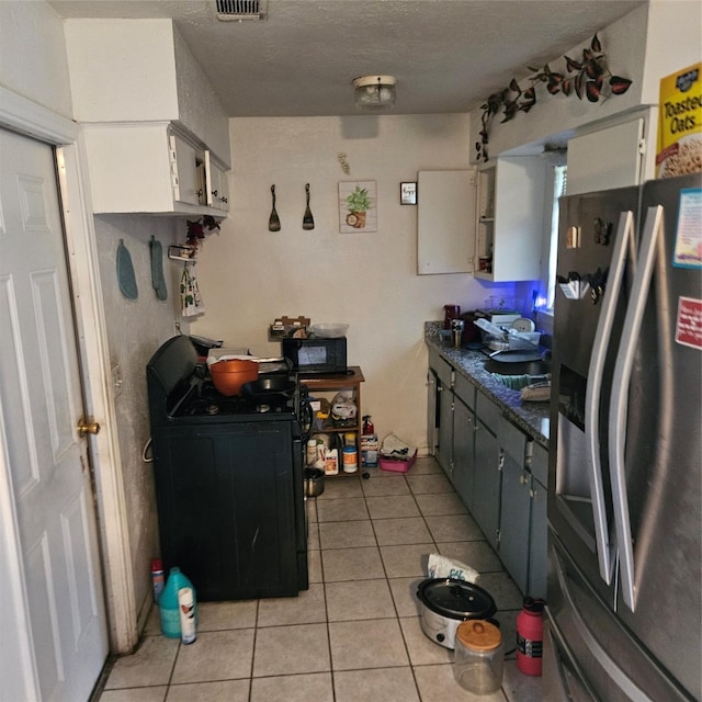 kitchen featuring light tile patterned flooring, stainless steel fridge with ice dispenser, white cabinetry, and black gas stove