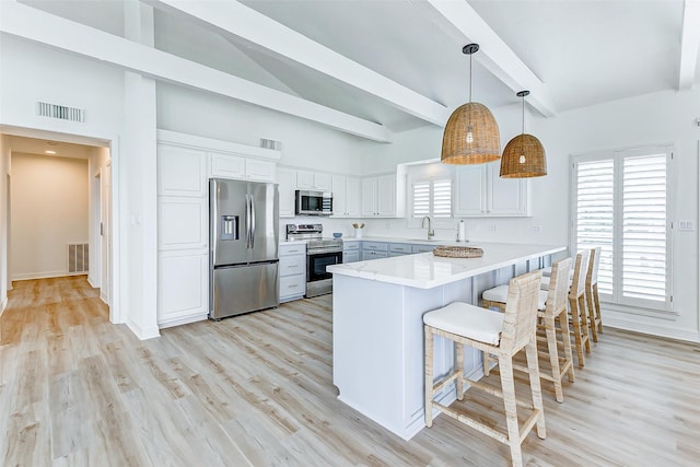 kitchen featuring white cabinetry, sink, stainless steel appliances, a kitchen breakfast bar, and decorative light fixtures