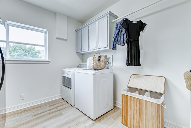 clothes washing area featuring washing machine and clothes dryer, cabinets, and light hardwood / wood-style floors