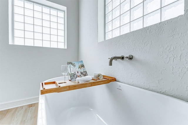 bathroom with a bathtub, a healthy amount of sunlight, and wood-type flooring