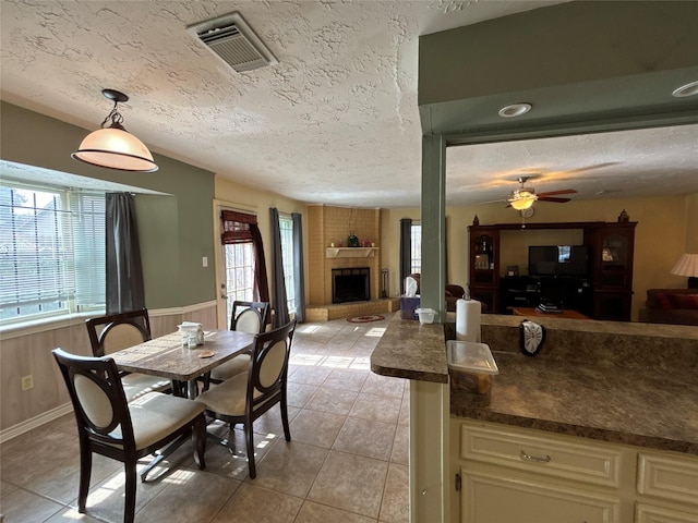 dining area featuring ceiling fan, a large fireplace, a textured ceiling, wooden walls, and light tile patterned floors