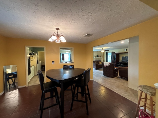 dining area with ceiling fan with notable chandelier, a textured ceiling, and dark tile patterned flooring