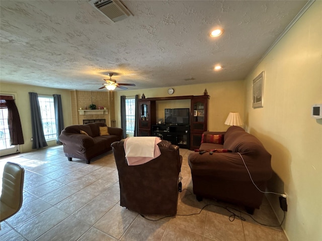 living room featuring ceiling fan, a fireplace, light tile patterned flooring, and a textured ceiling