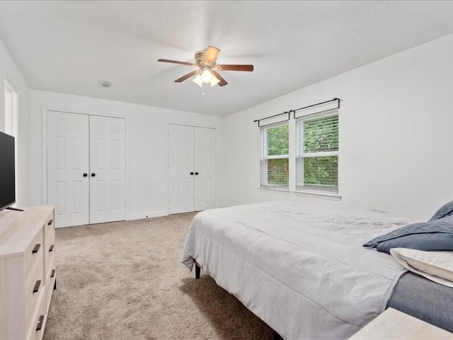 bedroom featuring multiple closets, ceiling fan, and light colored carpet