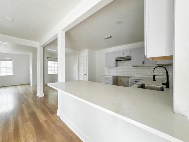 kitchen with sink, gray cabinets, decorative backsplash, kitchen peninsula, and light wood-type flooring