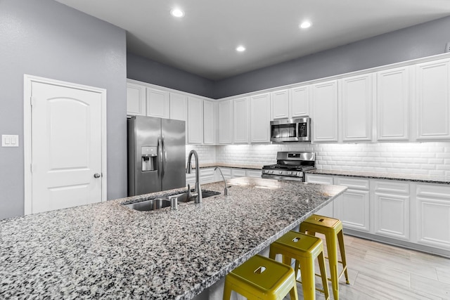 kitchen with sink, stainless steel appliances, dark stone counters, a breakfast bar area, and white cabinets