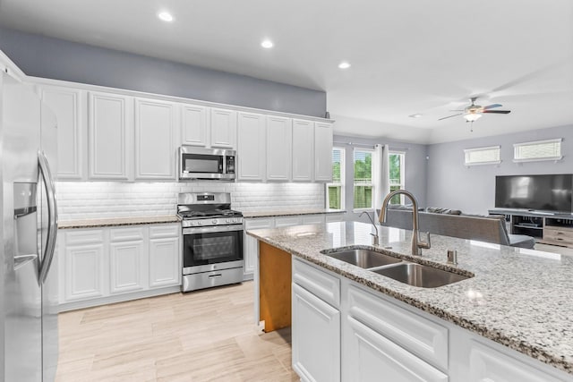 kitchen with appliances with stainless steel finishes, light stone counters, ceiling fan, sink, and white cabinets