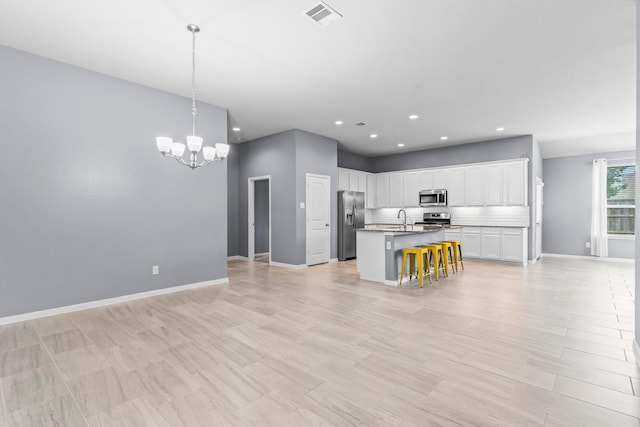 kitchen with backsplash, a center island with sink, appliances with stainless steel finishes, decorative light fixtures, and white cabinetry