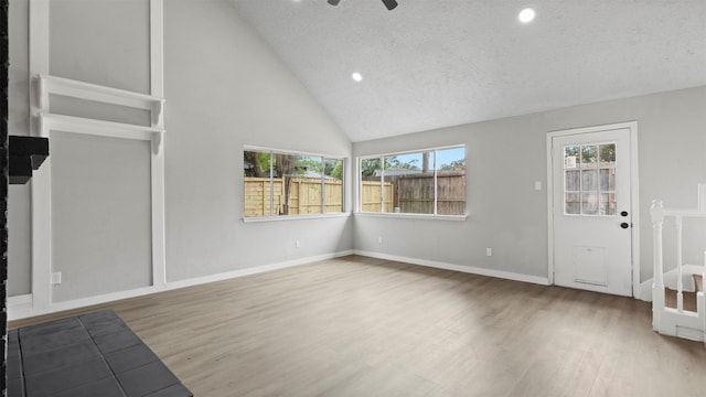 unfurnished living room with ceiling fan, high vaulted ceiling, a textured ceiling, and hardwood / wood-style flooring