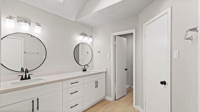 bathroom with vaulted ceiling, vanity, wood-type flooring, and a textured ceiling