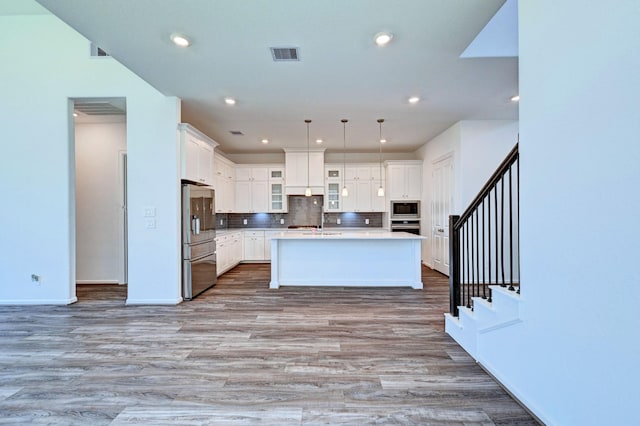 kitchen featuring a center island with sink, decorative light fixtures, white cabinets, and appliances with stainless steel finishes