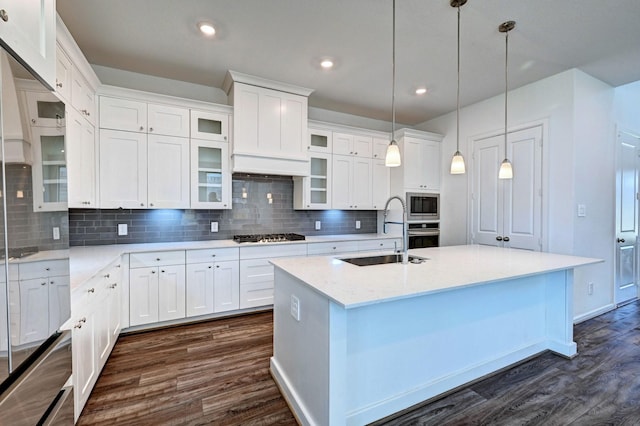 kitchen with built in microwave, sink, hanging light fixtures, a center island with sink, and white cabinets