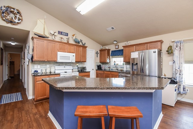 kitchen featuring a breakfast bar, a center island, vaulted ceiling, decorative backsplash, and appliances with stainless steel finishes